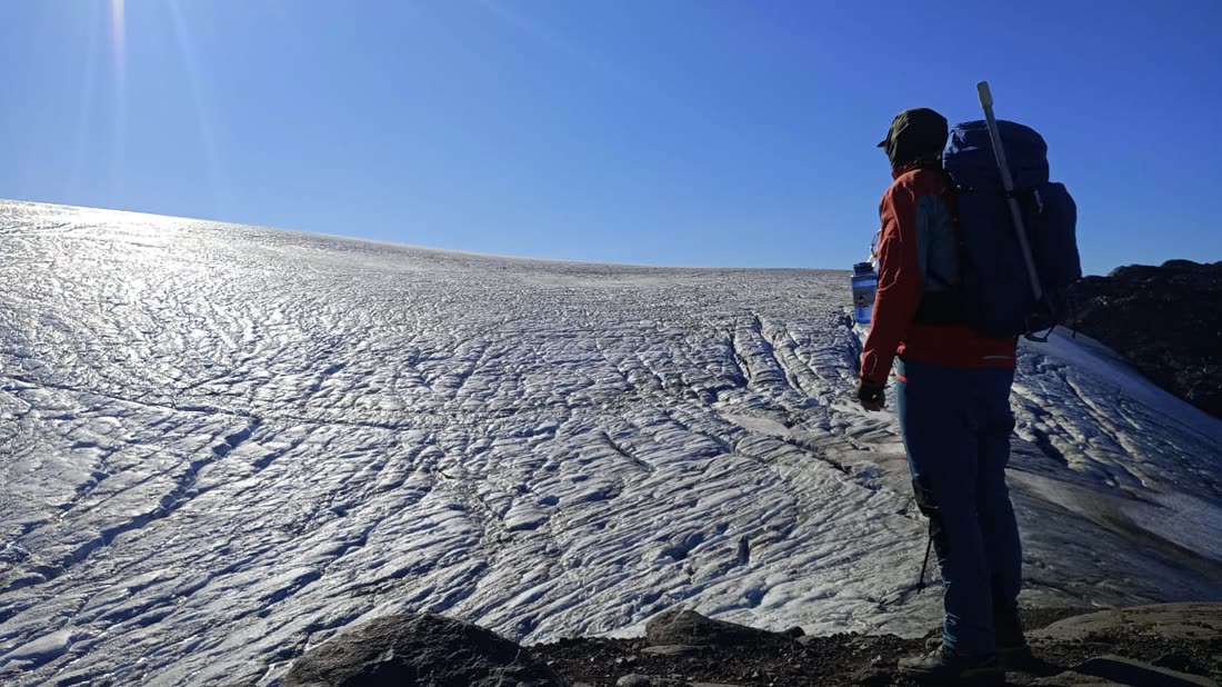 Montañista frente a un glaciar, con mochila y bastones, bajo el cielo despejado