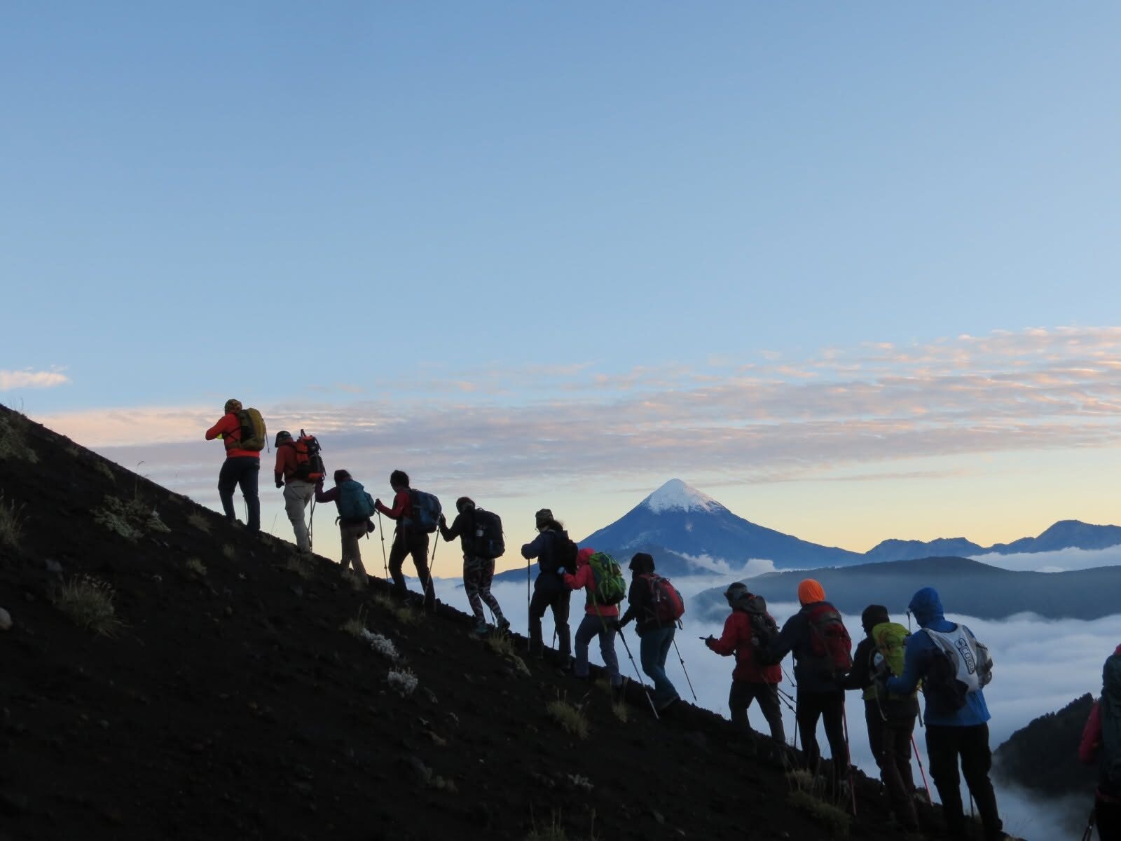 Grupo de montañistas subiendo al amanecer con el volcán Lanín de fondo